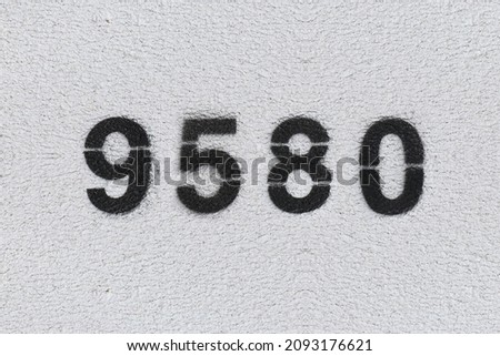 Black Number 9580 on the white wall. Spray paint. Number nine thousand five hundred and eighty.