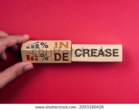 Decrease and increase percentage business concept. Words "INCREASE" on wooden block changing to "DECREASE," turning by hand with percentage symbol, growth and down chart graph icon on red background.
