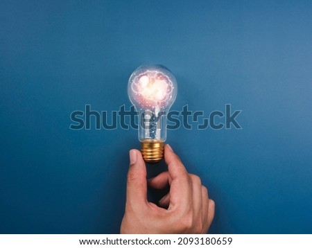 Creative, idea, innovation, knowledge, and inspiration concept. The human brain icon is glowing inside the digital light bulb in man's hand on the blue background, minimal style.