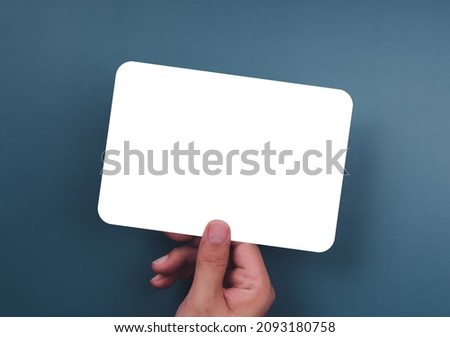 Mockup paper holding with the right hand. Hand holds the white blank mock-up white paper with a rounded corner and a horizontal style on a blue background.