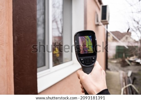 A male hand holds a thermal imager at the window of a house. Search for heat loss in private houses.