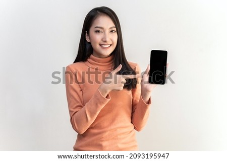 Portrait photo of young beautiful Asian woman pointing at black empty space on smart phone background can use for advertising or product presenting concept. Asian woman pointing at empty smart phone .