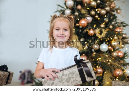 Charming little girl holds a gift on a background of Christmas trees