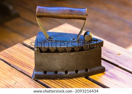 Vintage antique heavy cast iron retro iron with a wooden handle for ironing clothes is lying on a wooden table. Bric-a-brac collection at flea market. Retro technology, ancient steel tool for homework Royalty-Free Stock Photo #2093216434