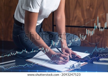 A woman trader in casual wear writing down some quotes to research stock market trends using smart phone for right investment. Wealth management concept. Hologram Forex chart over close up shot.