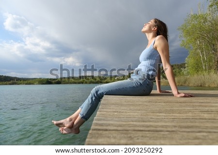 Side view portrait of a beautiful woman relaxing sitting in a pier Royalty-Free Stock Photo #2093250292