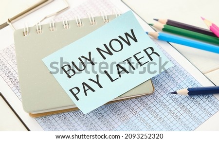 On a white table is a calculator, car key, cash, a pen and a notebook with the inscription BUY NOW - PAY LATER