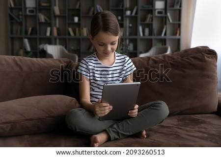 World of information. Curious kid preteen girl sit on sofa alone hold digital pad using gadget for learning browsing social networks chatting. Cute tween child schoolgirl play game on tablet pc online