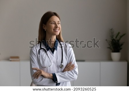 On guard of patients health. Confident optimistic young woman doctor nurse family therapist clinician stand in clinic office with crossed arms look at distance planning thinking dreaming. Copy space