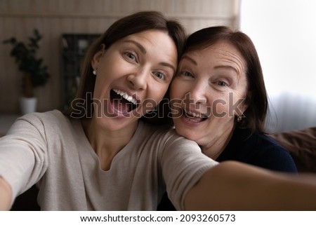 Kidding with mommy. Joyful grown daughter joking laughing taking funny selfie together with retired mother. Young and elderly women two sisters mom and adult child have fun at home shoot self portrait