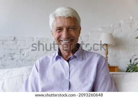 Portrait of smiling handsome hoary middle aged old 70s retired man sitting on couch at home. Happy relaxed mature senior grandfather looking at camera, holding video web call distant conversation. Royalty-Free Stock Photo #2093260648
