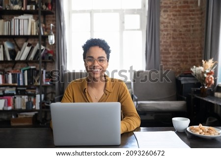 Portrait of happy young African American woman in eyewear sitting at table with computer. Smiling successful millennial female entrepreneur posing in modern loft style office room, feeling motivated. Royalty-Free Stock Photo #2093260672