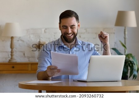 Emotional laughing happy young man looking at paper document, feeling excited reading amazing news, getting dream job offer, profitable deal or bank loan approvement, celebrating success at home. Royalty-Free Stock Photo #2093260732
