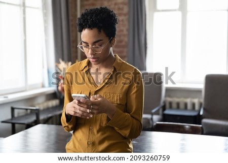 Frustrated serious young African American woman in eyewear looking at smartphone screen, feeling confused getting message or email with bad new, dissatisfied with bad device work, tech addiction. Royalty-Free Stock Photo #2093260759