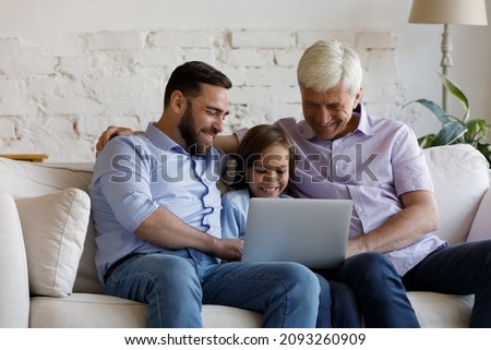 Happy bonding three male generations family using computer, sitting on couch, laughing preteen kid boy watching funny movie online with caring young father and smiling old retired grandpa at home.