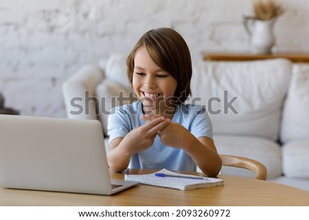 Happy teenage child boy looking at computer screen, making gestures, using sign language communicating online by video call with professional speech therapist, learning remotely alone at home.