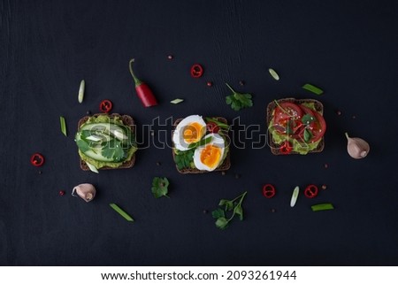 Delicious toast with guacamole, avocado, tomatoes, cucumbers and eggs on a black background