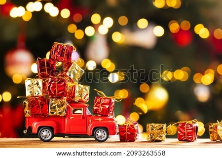 Red retro toy truck carries gifts on the background of Christmas tree with christmas lights. Concept of delivery of goods and a greeting card happy New year.