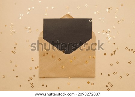 Craft brown envelope with black paper card over beige background and golden confetti