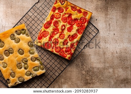 Two tipes of italian focaccia, with tomatoes and herbs and with olives on baking cooling rack. Brown background. Top view, copy space.