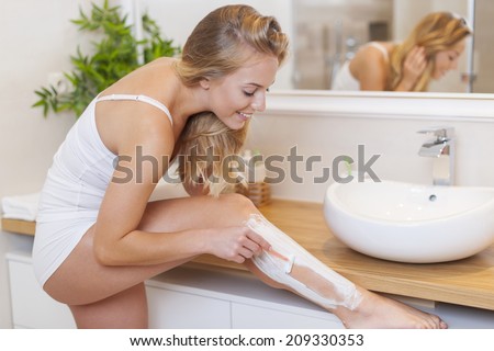 Beautiful blonde woman shaving legs in bathroom