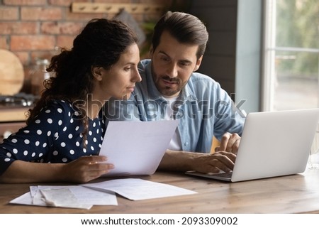 Focused young loving married couple discussing family savings, managing household budget, planning investment together, involved in financial paperwork, paying online using laptop e-banking app. Royalty-Free Stock Photo #2093309002