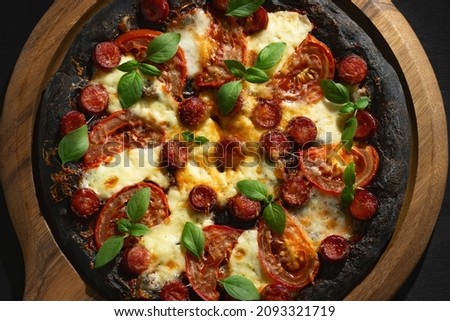 Black pizza with tomatoes, sausages, mozzarella and basil. Dough with healthy bamboo charcoal powder