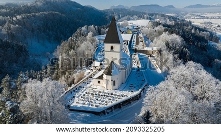 Photo of a snowy church in Austria , a beautiful view of snowy mountains, trees and a religous place.