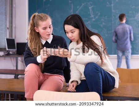 Girls students using smartphone during break in auditorium indoors