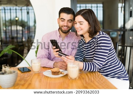 Excited couple in love making some online shopping on the smartphone and paying with a credit card at the cafe 