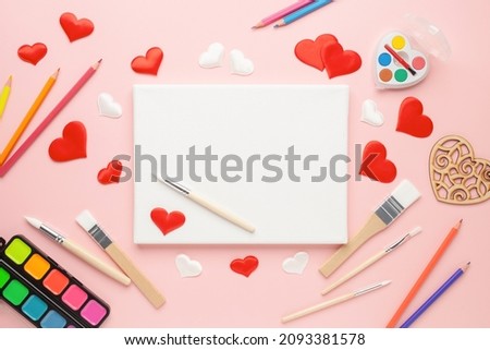 Valentine's Day concept. Canvas for paintings, brushes, paints and paper hearts on a pink background. Top View