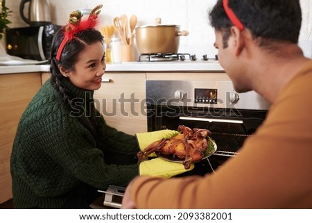 Young couple taking grilled chicken out of oven to serve for Christmas dinner