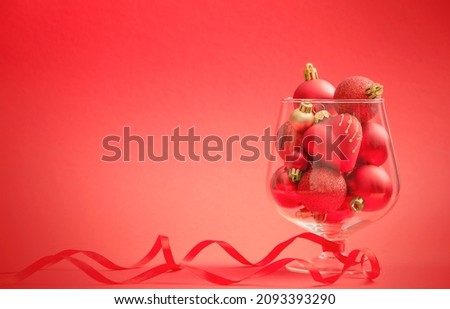 Big wineglass with red Christmas ornaments and red ribbon on red background