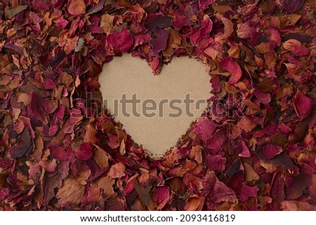 Heart in a background of dried red rose petals. Love, Valentine's day card. Heart shape and dry roses petals backdrop, copy space