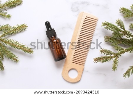 Natural hair care flat lay, wooden hair comb and oil with fir branches on marble background