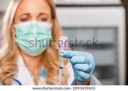A Young Female Medical Doctor Extracting a Covid-19 Vaccine Injection with a Syringe Needle Wearing Gloves, Surgical Protective Mask, White Lab Coat and Stethoscope in Hospital or Health Clinic.