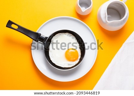 Scrambled, frying  eggs from one egg in a small pan on yellow ba Royalty-Free Stock Photo #2093446819