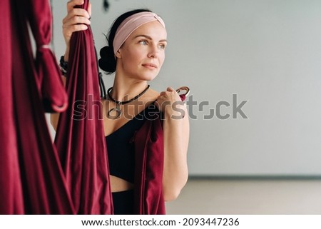 A woman fastens a hook from a hanging hammock for yoga in the gym.