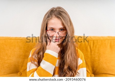 Portrait of a beautiful funny girl with glasses, nerd Schoolgirl in big eyeglasses on a yellow sofa