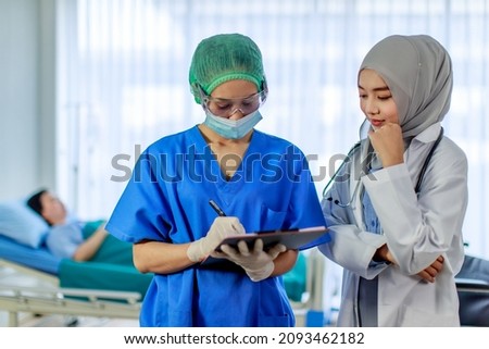 Asian professional female nurse in blue hospital uniform and Muslim Islam Arab doctor discussing writing checkup symptom on clipboard while senior woman patient resting sleeping in blurred background.
