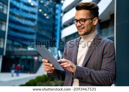 Happy young business man with tablet at work in modern urban background