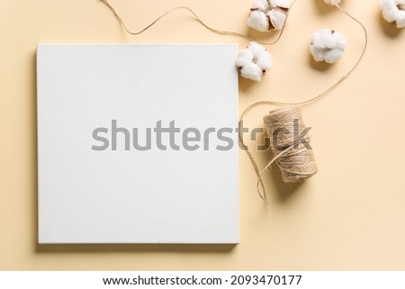 Blank poster, rope and cotton flowers on color background