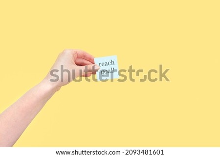 The hand holds a sticky note with inscription Reach goal! Motivational statement. Royalty-Free Stock Photo #2093481601