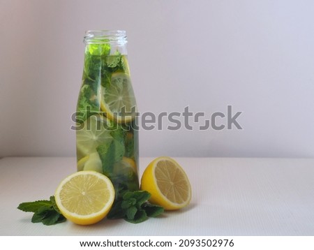 Detox water with lemon slices, fresh mint leaves and ginger slices in a glass bottle, supplemented with fresh lemon halves and mint sprigs. Isolated on white, copy space