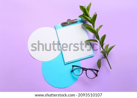 Clipboard with blank sheet of paper, cards, eyeglasses and plant branch on color background