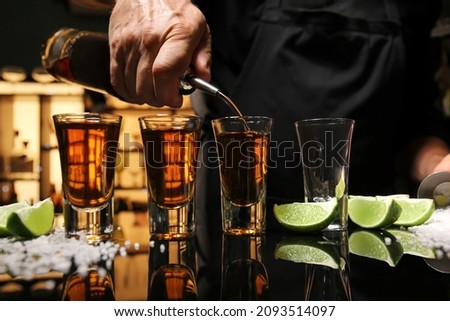Bartender pouring tasty tequila into glasses at table in bar Royalty-Free Stock Photo #2093514097