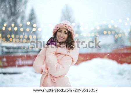 Merry young woman wears knitted cap walking at the holiday fair against the background of garlands. Empty space