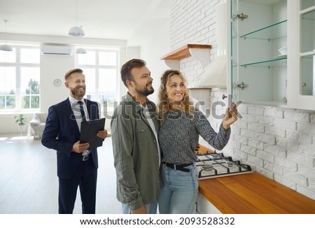 Realtor with customers checking apartmnet. Couple examines furniture in kitchen while inspecting house with real estate agent. Friendly male realtor advises young family before buying new home. Royalty-Free Stock Photo #2093528332