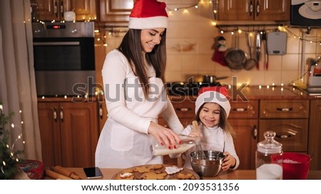 Mom with adorable little daughter spend time at kitchen in Christmas eve. Girls preparing sweets for holidays. Gingerbread and candy. Happy family