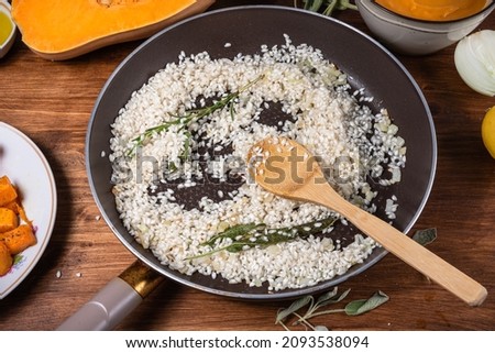 Preparing risotto with pumpkin - raw rice fried in a pan with sage and ingredients for cooking around.
